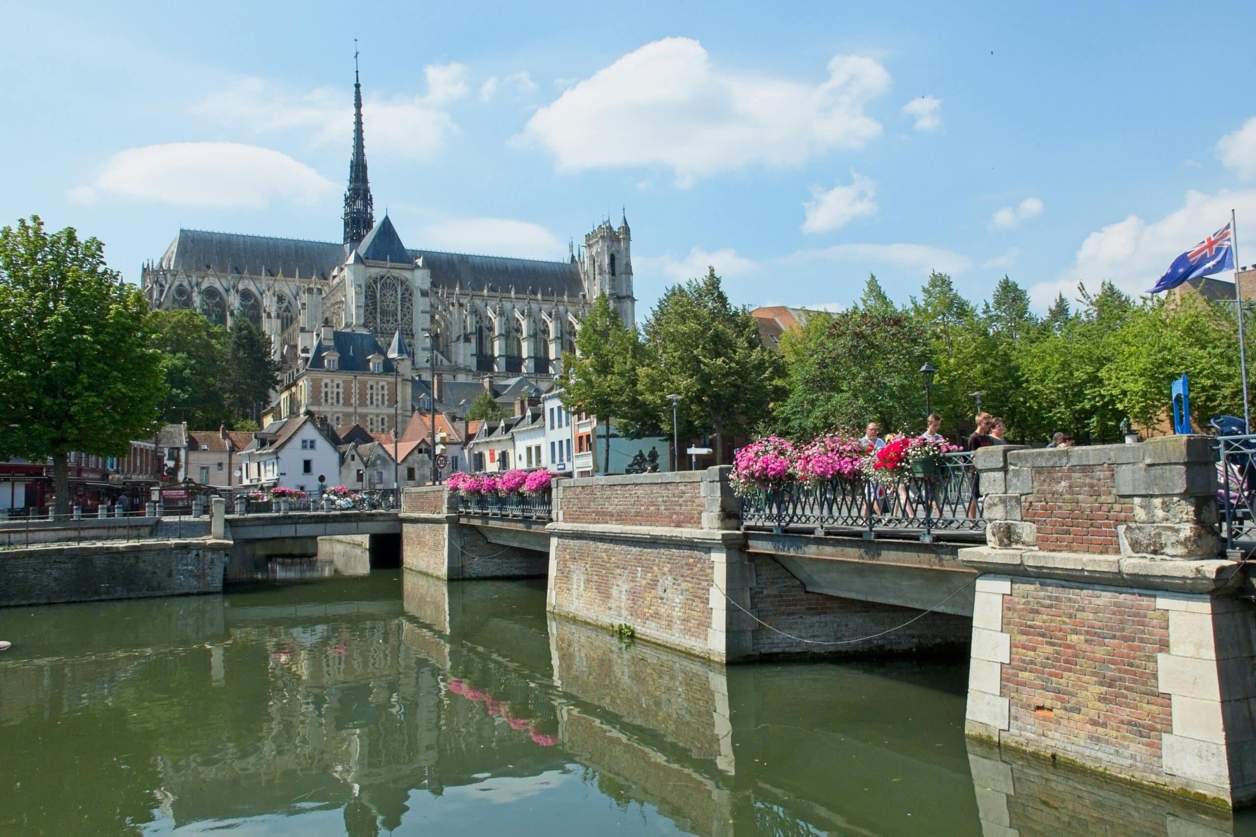 Charming view of Amiens Cathedral and bridge with summer reflections and flowers.